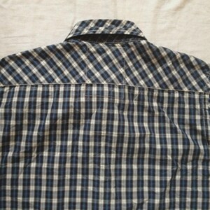 May include: Back view of a blue, black, and white plaid button-down shirt. The shirt has a collar and a yoke detail. The fabric is a woven cotton or similar material. The shirt is likely a casual wear item.
