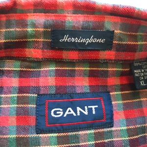 Puede incluir: Primer plano de una camisa a cuadros roja, verde y azul con la marca "GANT" en un parche azul. La camisa tambi&eacute;n tiene una etiqueta "Herringbone" y una etiqueta que indica XL/TG.
