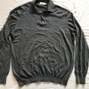 Puede incluir: Una camisa polo de manga larga gris con cierre de botones. La camisa está hecha de un material suave y cómodo.