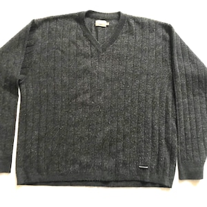 Puede incluir: Un suéter gris oscuro con cuello en V y detalles acanalados verticales. El suéter de manga larga tiene una pequeña etiqueta cerca del escote y una pequeña etiqueta cerca del dobladillo inferior. El suéter está hecho de un material suave y texturizado.