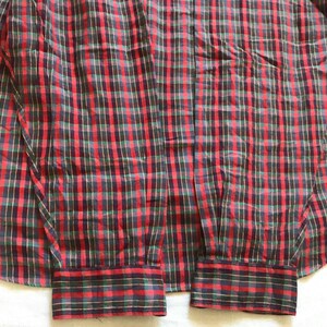 Puede incluir: Una camisa a cuadros roja, negra y verde. Los pu&ntilde;os son visibles y la tela presenta un dise&ntilde;o de cuadros cl&aacute;sico. La camisa est&aacute; hecha de un material ligero, adecuado para ropa informal.