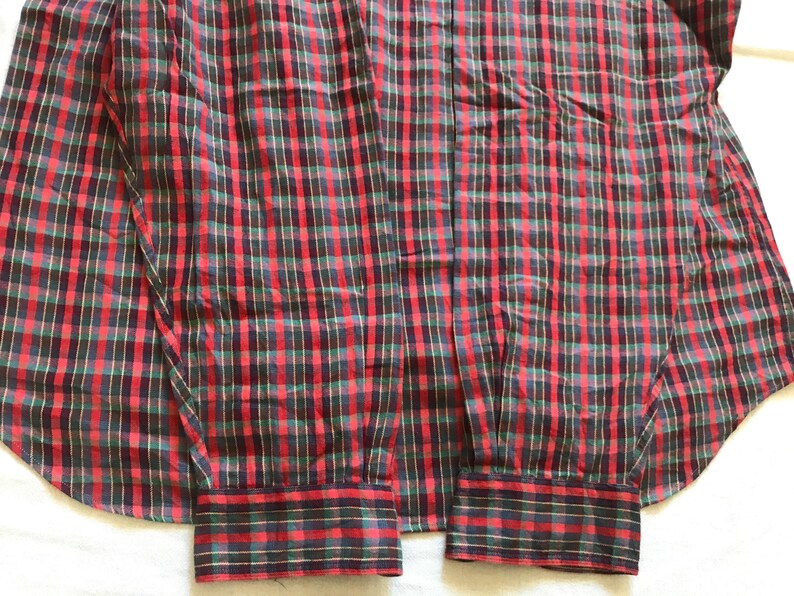 Puede incluir: Una camisa a cuadros roja, negra y verde. Los pu&ntilde;os son visibles y la tela presenta un dise&ntilde;o de cuadros cl&aacute;sico. La camisa est&aacute; hecha de un material ligero, adecuado para ropa informal.