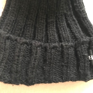 May include: Close-up of a black knit beanie hat. The hat has a ribbed design and a folded brim. A small black tag with a white "H" is attached to the brim. The hat appears to be made of a thick, warm material.
