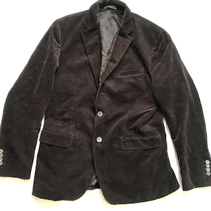 May include: A dark brown corduroy blazer with a two-button closure and a notched lapel. The jacket has two front pockets and buttons on the sleeves. The blazer is a classic style, suitable for various occasions.