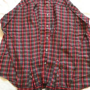 Puede incluir: Una camisa a cuadros roja, negra y verde con cuello y mangas largas. La camisa tiene botones plateados y la marca "GANT" es visible en el cuello. La camisa est&aacute; hecha de una tela ligera.