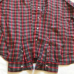 Puede incluir: Una camisa a cuadros roja, verde y negra. Tiene mangas largas con pu&ntilde;os abotonados y un cuello cl&aacute;sico. La camisa est&aacute; hecha de tela tejida y tiene botones plateados.