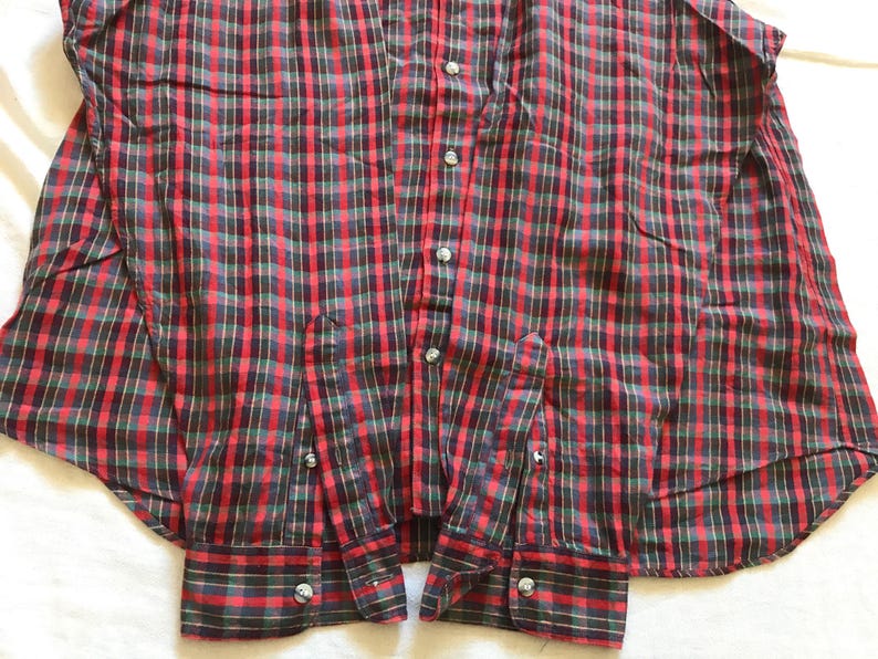 Puede incluir: Una camisa a cuadros roja, verde y negra. Tiene mangas largas con pu&ntilde;os abotonados y un cuello cl&aacute;sico. La camisa est&aacute; hecha de tela tejida y tiene botones plateados.