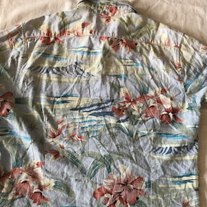 May include: A light blue short-sleeved shirt with a tropical print featuring pink and red flowers, green leaves, and a beach scene.