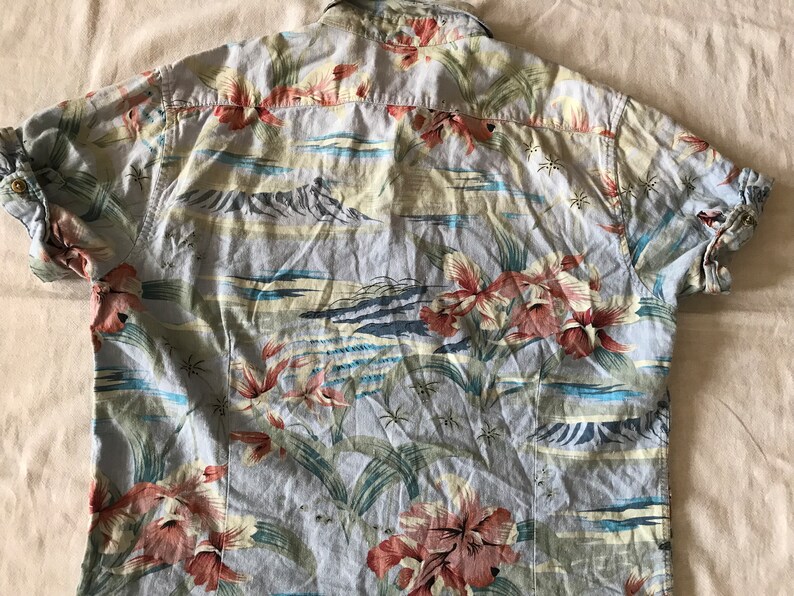 May include: A light blue short-sleeved shirt with a tropical print featuring pink and red flowers, green leaves, and a beach scene.