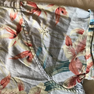 May include: A light blue short-sleeved shirt with a floral print featuring pink, red, and green flowers. The shirt has a button-up closure and a collar.