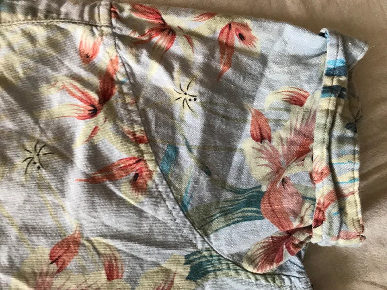 May include: A light blue short-sleeved shirt with a floral print featuring pink, red, and green flowers. The shirt has a button-up closure and a collar.