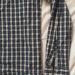 May include: A long-sleeved plaid shirt in shades of navy blue, white, and light blue. The shirt features a button-down cuff and a chest pocket. The fabric has a classic checkered pattern.