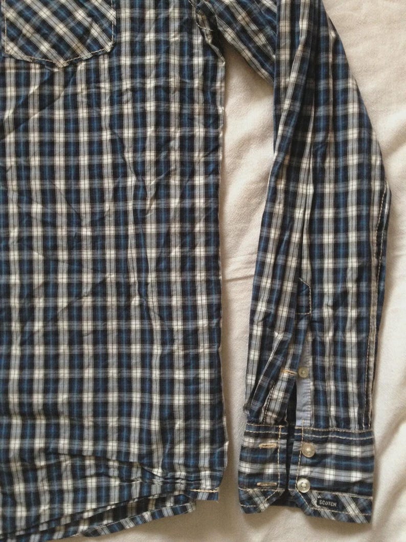 May include: A long-sleeved plaid shirt in shades of navy blue, white, and light blue. The shirt features a button-down cuff and a chest pocket. The fabric has a classic checkered pattern.