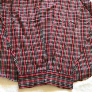 Puede incluir: Una camisa a cuadros roja, negra y verde. La camisa de manga larga tiene un cuello cl&aacute;sico. El patr&oacute;n de cuadros es un dise&ntilde;o tradicional, con los colores dispuestos en una cuadr&iacute;cula. Los pu&ntilde;os tambi&eacute;n son a cuadros.