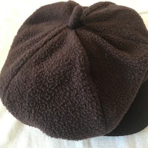 Könnte beinhalten: Eine braune Mütze aus Fleece im Newsboy-Stil mit schwarzem Schirm.