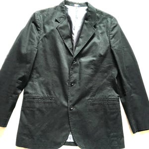 May include: A black blazer with a three-button fastening and two front pockets. The blazer features a notched lapel and a light-coloured lining. The jacket is made of a smooth, possibly satin-like material.