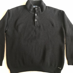 May include: A black ribbed sweater with a mock neck and a button closure. The sweater has long sleeves and a relaxed fit.