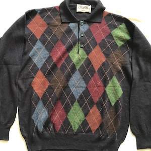 May include: A navy blue long-sleeved sweater with a diamond pattern in shades of red, green, brown, and blue. The sweater has a button-up collar and a small label that reads "Danny & Mark" on the front.
