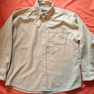 May include: A beige long-sleeve button-down shirt with a single chest pocket.