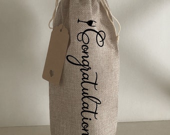 May include: A beige burlap wine bottle bag with a brown paper gift tag and the text "Congratulations" printed in black.
