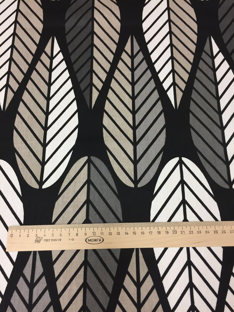 May include: Black fabric with a repeating pattern of white, gray, and beige stylized leaves. The fabric is measured with a ruler in inches.