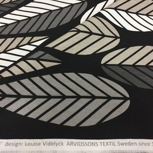 May include: Black fabric with a repeating pattern of stylized leaves in shades of gray, white, and beige. The fabric has a white label with the text "BLADER" design: Louise Videlyck ARVIDSSONS TEXTIL Sweden since 1949.