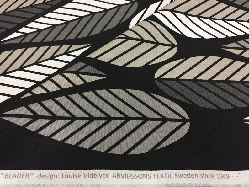 May include: Black fabric with a repeating pattern of stylized leaves in shades of gray, white, and beige. The fabric has a white label with the text "BLADER" design: Louise Videlyck ARVIDSSONS TEXTIL Sweden since 1949.
