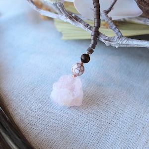 May include: A pink rose quartz crystal pendant on a brown beaded necklace with a white and brown bead.