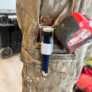 May include: A carpenter's work shorts with paint splatters, a tape measure, and a blue pencil held in a white clip. The tape measure is red and black. The shorts are tan.