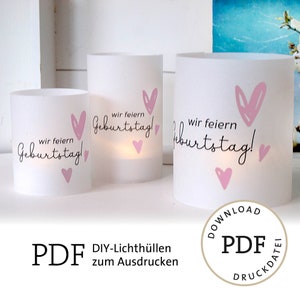 Op de afbeelding: Drie witte kaarsenhouders met roze harten en de tekst "wir feiern Geburtstag!" erop gedrukt. De kaarsenhouders staan op een wit oppervlak. De afbeelding is een downloadbare PDF om te printen.