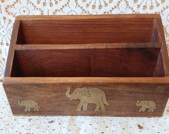 May include: A wooden letter holder with two compartments and a decorative design of three brass elephants. The elephants are in a line, with the largest elephant in the center and two smaller elephants on either side.