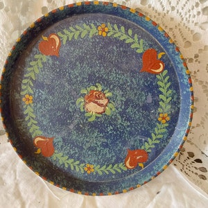 May include: A blue metal tray with a painted design of red hearts, green leaves, yellow flowers, and a white rose in the centre.