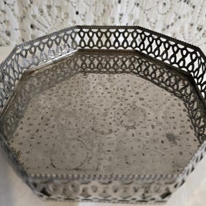 Può includere: Un vassoio vintage in metallo argentato di forma ottagonale. Il vassoio presenta una superficie strutturata e un bordo decorativo traforato. Il vassoio viene probabilmente utilizzato per servire o esporre.