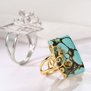 May include: Two rings, one silver and one gold. The silver ring has a delicate, openwork design. The gold ring features a large, rectangular turquoise stone with black veins.