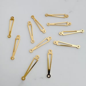 May include: A collection of gold-colored jewelry connectors. The connectors have a geometric design with a triangular shape and small holes at each end for attaching to other jewelry components. The connectors are scattered on a white surface.