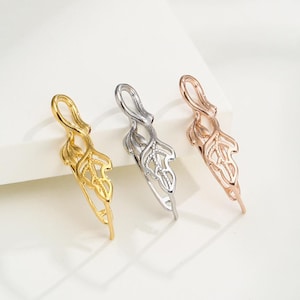 Puede incluir: Tres hallazgos de joyería metálicos en forma de hoja en oro, plata y oro rosa. Cada uno tiene un lazo en la parte superior y un diseño de hoja detallado. Los hallazgos se muestran sobre una superficie blanca.