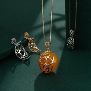 May include: A selection of necklaces with pendants. One necklace has a gold chain with a round, amber-coloured pendant in a decorative gold filigree. Other pendants include silver and gold crescent moon designs.