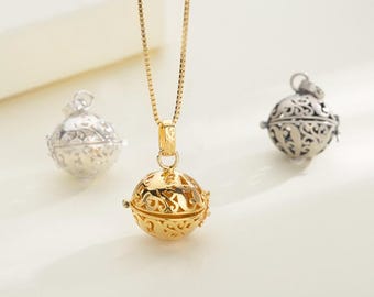 May include: A gold-toned necklace featuring a spherical pendant with an intricate openwork filigree pattern. Two additional spherical pendants with the same filigree design are present, one in a silver tone and one in a dark metallic finish.