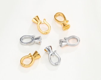 May include: A selection of gold and silver-coloured jewellery clasps. The clasps feature a distinctive design with a flared base and a curved, hook-like top. The clasps are presented against a white backdrop, highlighting their metallic shine.