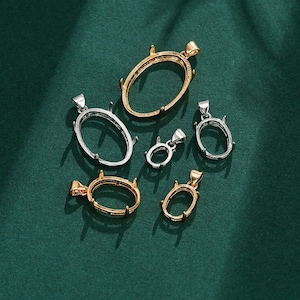 May include: An assortment of oval-shaped pendant settings in gold and silver tones. The settings are empty, designed to hold gemstones. The pendants are displayed on a dark green surface, showcasing their design and potential use in jewelry making.