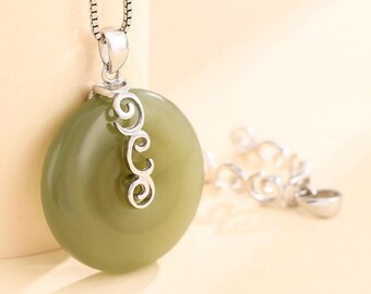Può includere: Collana con pendente rotondo verde oliva e catena argentata. Il pendente presenta un dettaglio decorativo argentato. La collana è mostrata su uno sfondo chiaro.