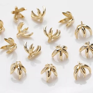 Op de afbeelding: Goudkleurige metalen bloemvormige sieradenonderdelen. De onderdelen hebben een driedimensionaal ontwerp met meerdere bloemblaadjes. De onderdelen zijn verspreid over een wit oppervlak. Ideaal voor het maken van sieraden.