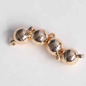 May include: Gold-toned magnetic clasp for jewelry making. The clasp is made of four round metal balls connected together.