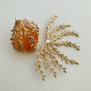 Puede incluir: Dos adornos de metal en forma de hoja de color dorado. Uno es un diseño en forma de jaula y el otro es un diseño más abierto y más grande con múltiples ramas.