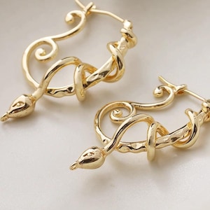 May include: A pair of gold-coloured hoop earrings. Each earring features a stylised snake design, with a coiled body and a pointed head. The earrings have a polished finish and a secure clasp.