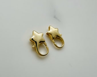 May include: Two gold-toned star-shaped clasps for jewelry making. The clasps are made of metal and have a shiny finish.
