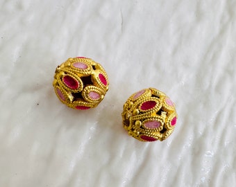 Peut inclure: Deux perles rondes de couleur dorée avec des accents en émail rose et rouge. Les perles ont un motif décoratif de petites pièces ovales.