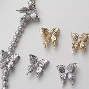 May include: Five silver and gold butterfly charms with clear rhinestone accents. The charms are on a white background.