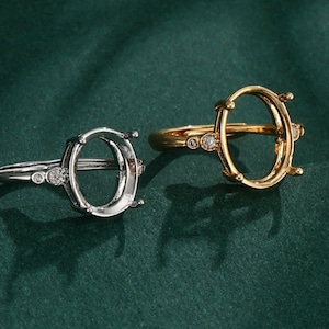 Pode incluir: Duas engastes de anel ovais com pequenas pedras transparentes na banda. Um engaste é de prata e o outro de ouro.