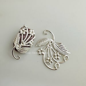 May include: Two silver floral embellishments with a delicate, intricate design. Each piece features a cluster of small flowers and a leaf, perfect for adding a touch of elegance to jewellery or crafts.